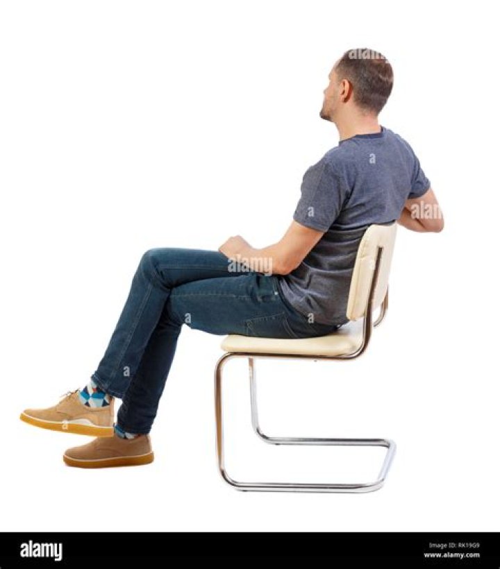 a man sitting in a chair with a guitar on his lap and wearing a hat